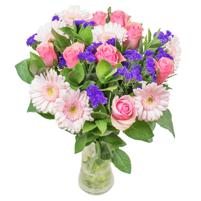 An expressive floral arrangement artfully presented in a pristine, clear glass vase, distinct against a pure white background that accentuates every textural nuance. At its heart are seven to nine blush to medium pink roses, their petals in various stages of bloom highlighting the classic spiral so beloved in English garden design. These are complemented by five to seven airy pale pink Gerbera daisies-large, sun-like heads with near-white centres, humming with gentle elegance. Here and there, clusters of vibrant purple statice (or possibly Limonium) create eye-catching percussive highlights, lending playful movement and a rich counterbalance to the softer shades. The ensemble is cradled by deeply green foliage, full and glossy, recalling the lushness of Winchmore Hill's many parks and green spaces. The transparent vase, revealing neat stems and fresh water, completes the image-suggesting the immediacy and quality of a same-day delivery from Winchmore Hill Florist. Perfect for marking special occasions-birthdays, Mother's Day, or heartfelt anniversaries-or simply to add a touch of brightness and warmth to any home or workspace in N21.